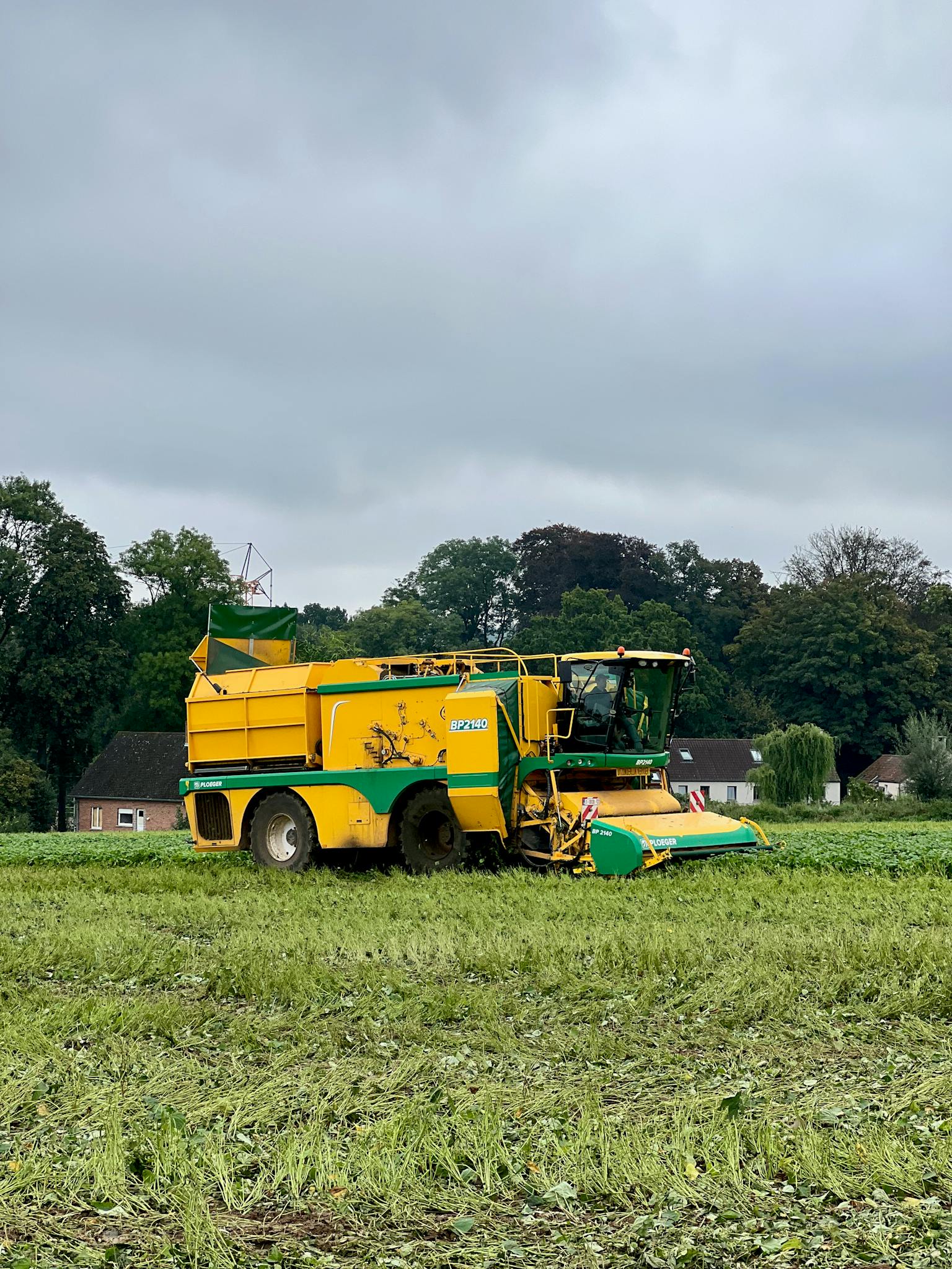 A yellow harvester working in a rural field under an overcast sky, showcasing agricultural machinery.